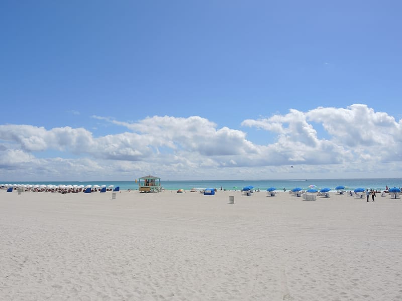Miami Beach: sandy beach with lifeguard station, umbrellas, beachgoers, ocean and clouds