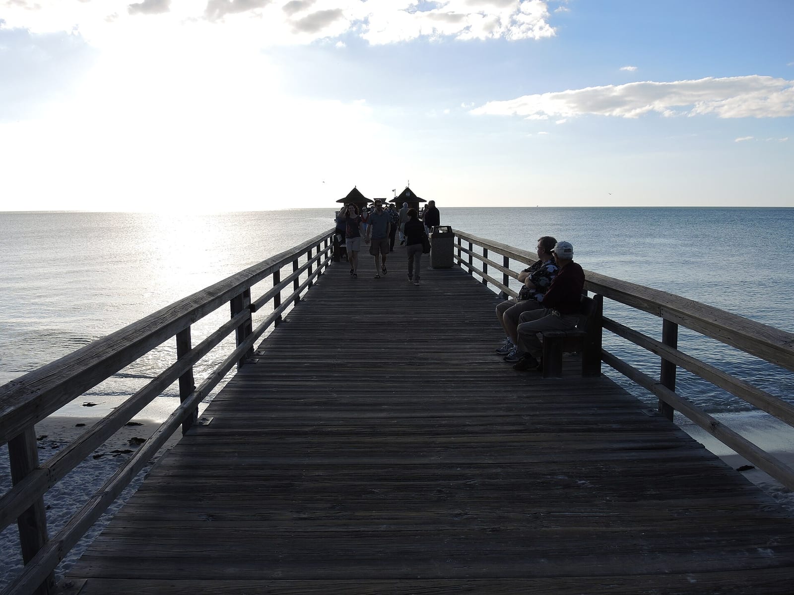 16th Avenue South Beach: wooden pier extending into calm ocean with distant figures and pavilion