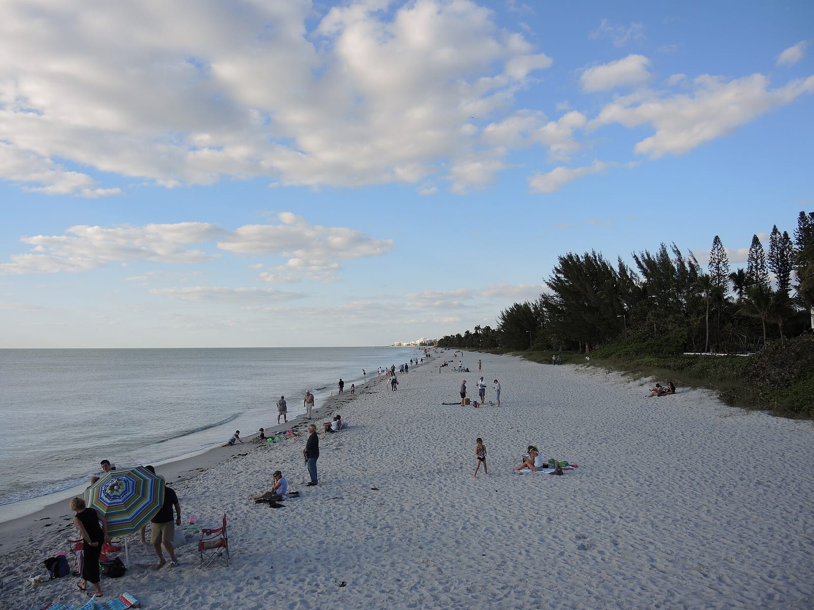 5th Avenue South Beach: sandy beach with scattered visitors, calm water, trees, cloudy sky