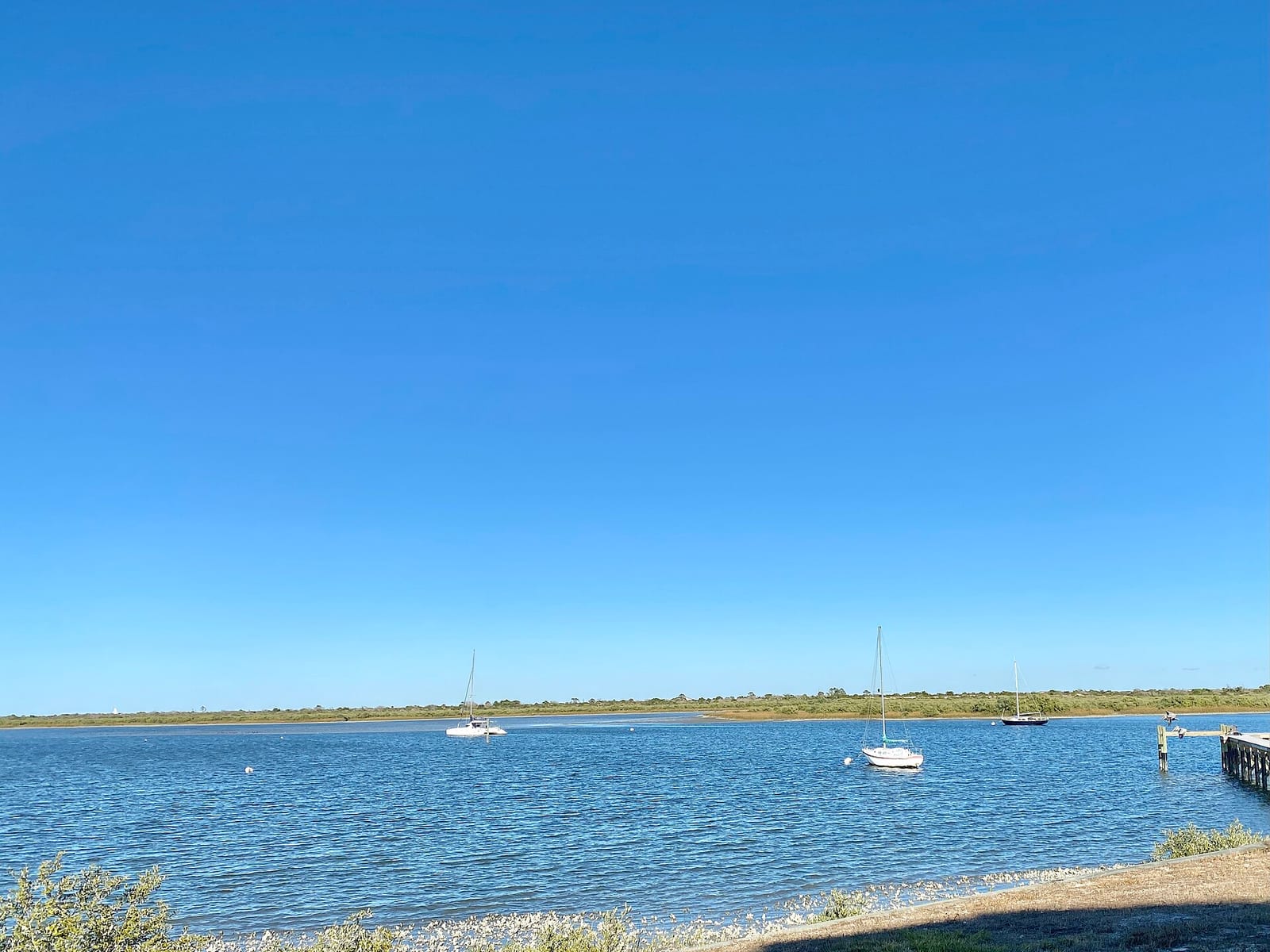 Anastasia State Park: sailboats anchored in blue water with sandy shore and marsh grass