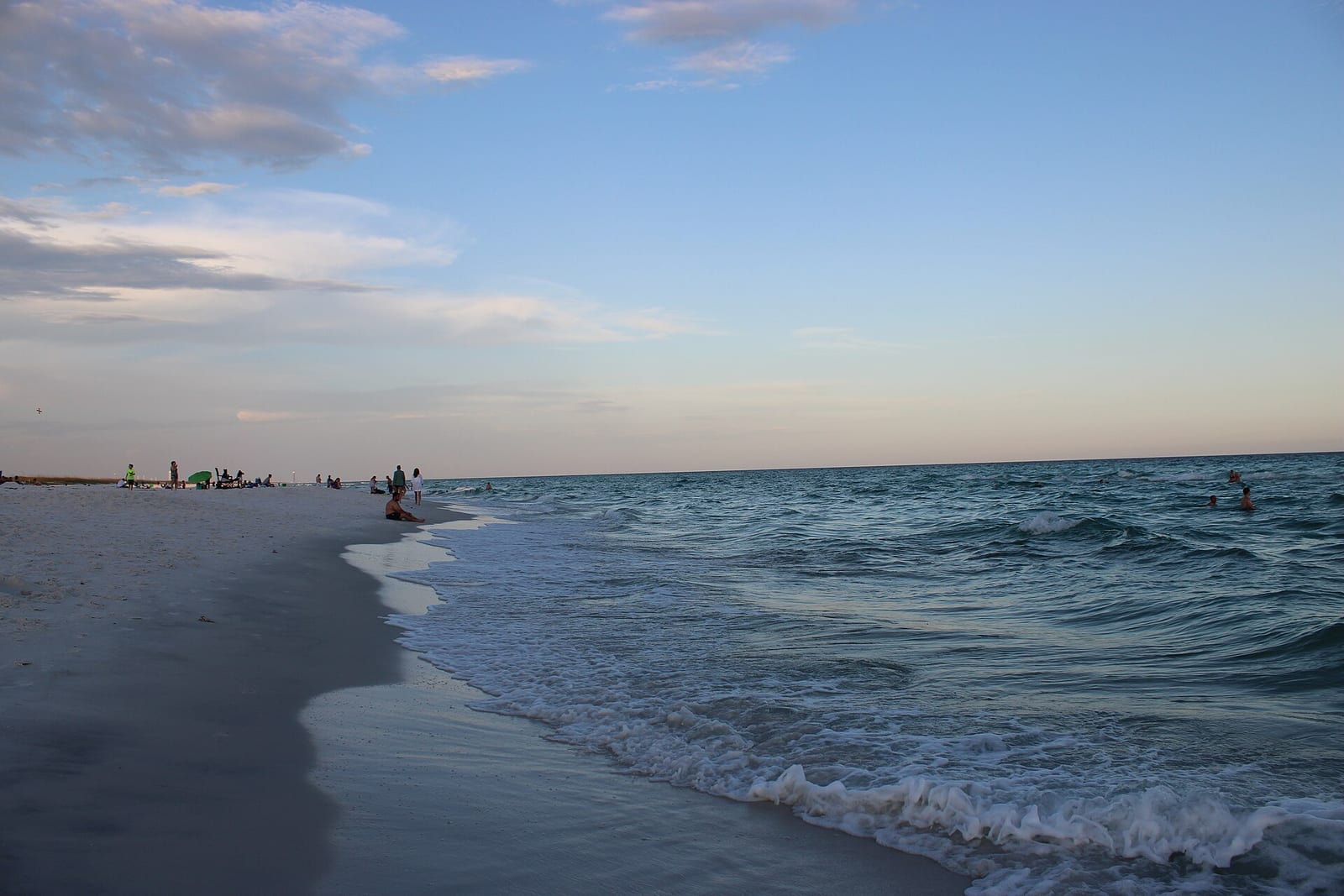 Navarre Beach: beach shoreline with waves, sand, and distant swimmers at dusk