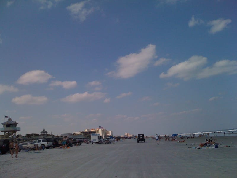 New Smyrna Beach: wide sandy beach with vehicles, beachgoers, water, and coastal buildings