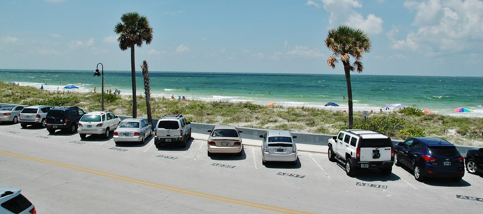 Pasa A Grille Beach: parking lot with cars overlooking beach with palm trees and ocean