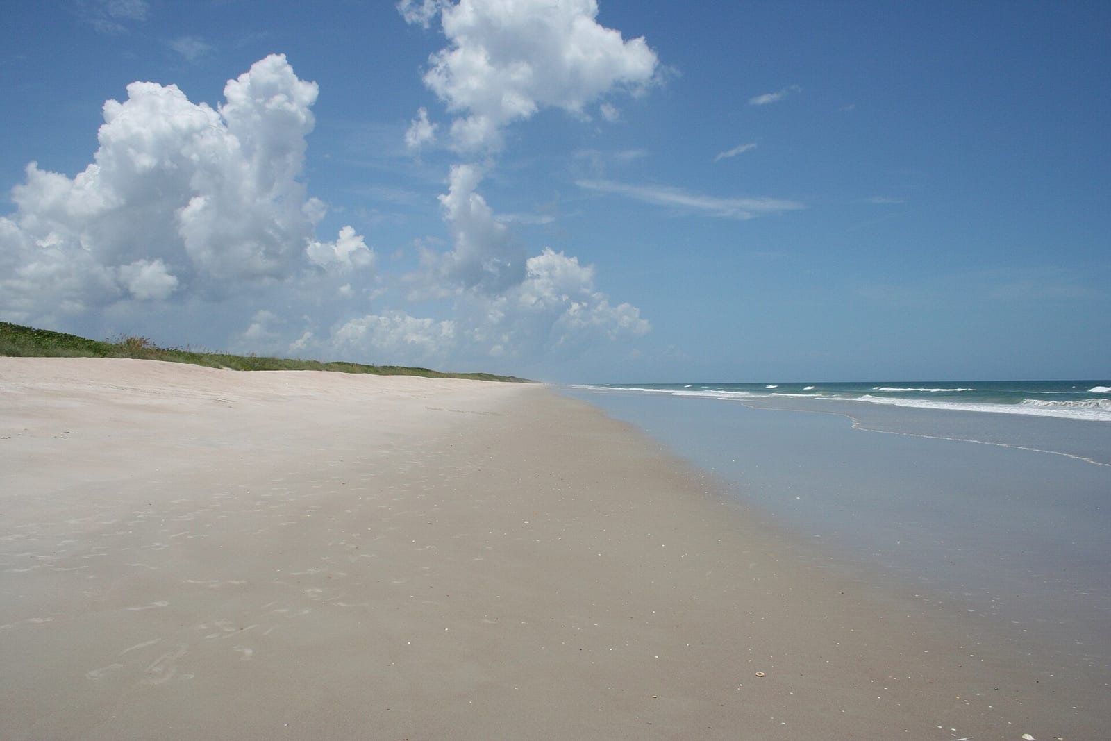 Playalinda Beach: wide sandy beach with dunes, calm water, and blue sky with clouds