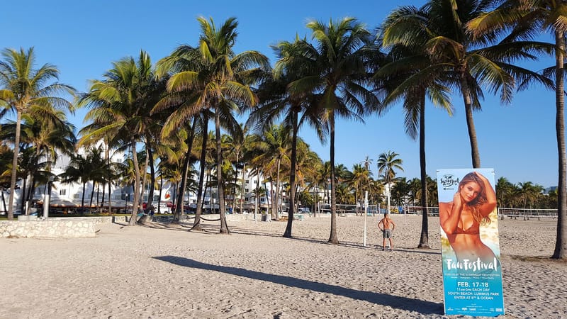 Sandy's Beach: sandy beach with palm trees, buildings, and festival banner